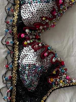 Handgjord paljett-bh med pärlor - Unik bh dekorerad med paljetter i silver och svart,  mängder av färgglada pärlor och söt liten pärlfrans mitt fram. Bas i svarta paljetter med kant av guldpaljetter runt om och justerbara axelband. Så snyggt under en kavaj eller genomskinlig blus, ett riktigt statement-plagg. Det står stl M men den är mer som en S