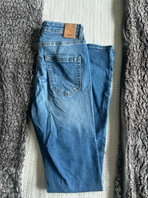Blå jeans från ONLY - Snygga blå jeans från ONLY med klassisk femficksdesign och skinnpatch bak i midjan. Jeansen har en rak passform och är tillverkade i ett mjukt denimtyg som ger en bekväm känsla. Perfekta till vardagslooken och lätta att matcha med olika stilar.