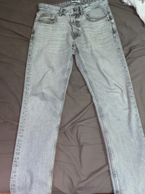 Grå tvättade jeans från Zara - Säljer ett par grå tvättade jeans från Zara med klassisk femficksmodell och raka ben. Jeansen har en snygg vintagekänsla och är tillverkade i bomull. Perfekta för dig som gillar en avslappnad men trendig stil.