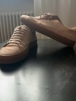  sneakers från Axel Arigato - Snygga  sneakers från Axel Arigato i mocka med matchande rost rosa skosnören och bruna gummisulor. Stilren low-top modell med minimalistisk design och diskret logga på sidan. Perfekta för dig som gillar en clean och modern look. Pris kan diskutera! Så hör av dig!