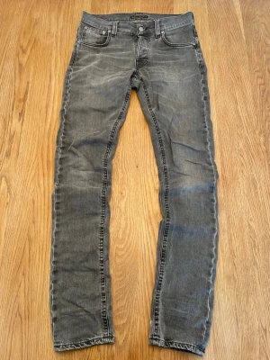 Nudie jeans - Grå jeans från Nudie i modell Tilted Tor med slitningar. Normal midja, dragkedja och knappstängning. Perfekta för en avslappnad och trendig look. Inga defekter, strl W29 L32
