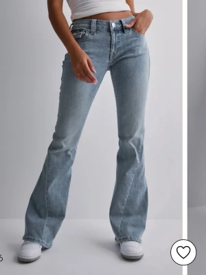 Ljusblå bootcut jeans från True Religion - Säljer ett par ljusblå bootcut jeans från True Religion med klassiska kontrastsömmar och snygga fickdetaljer bak. Jeansen har låg midja och är tillverkade i denim med lätt tvättad look. Perfekta för dig som gillar retrovibbar och vill ha en avslappnad men trendig stil.