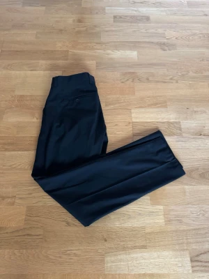 Svarta kostymbyxor med rak passform - Snygga svarta kostymbyxor med klassisk rak passform och pressveck. Byxorna har en enkel knappstängning i midjan och är perfekta för en stilren look. Materialet känns mjukt och följsamt, vilket gör dem bekväma att bära hela dagen.