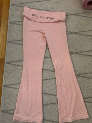 Rosa mjukisbyxor Juicy Couture - Använts 0 gng men säljer dessa för behöver pengar just nu men kommer sakna dem. ett par ljusrosa mjukisbyxor från Juicy Couture med utsvängda ben, vikbar midja där loggan står tryckt på baksidan . Byxorna är i mjukt och stretchigt material, perfekta för chill dagar, gym, skoloutfit.