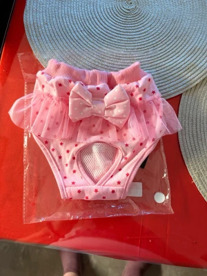 Söt rosa hund trosor med rosett och stjärnor - Supersöt rosa hund  trosa med små röda stjärnor, volang i tyll och en stor prickig rosett framtill. Trosan har elastisk midja och meshdetalj framtill. Perfekt för dig som gillar gulliga detaljer och lekfull stil.