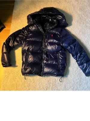 Mörkblå dunjacka med huva Polo Ralph Lauren - Säljer en mörkblå dunjacka/vinterjacka  från Polo Ralph säljer pågrund av att börjar bli liten passar mellan 170-185 hör av er vid frågor ! 