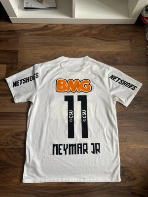 Vit Santos Neymar Jr matchtröja - Säljer en vit Santos FC matchtröja från Nike med Neymar Jr och nummer 11 på ryggen. Tröjan har flera sponsorloggor, bland annat BMG, Netshoes och Seara, samt klubbmärke på bröstet. Tillverkad i Dri-FIT material som andas och har korta ärmar.