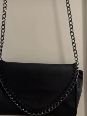 Svart axelväska med kedjerem - Fin väska i ganska bra skick, lite defekter på den då den är köpt på loppis