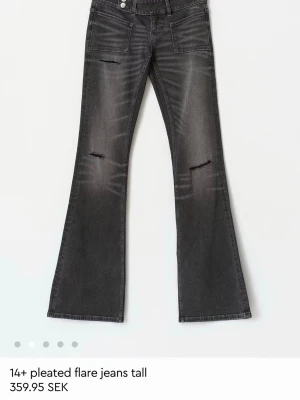 Grå utsvängda jeans med slitningar - Snygga grå jeans med utsvängda ben och slitna detaljer på låren. Jeansen har framfickor och markerade sömmar som ger en cool look. Perfekta för dig som gillar en trendig och avslappnad stil.