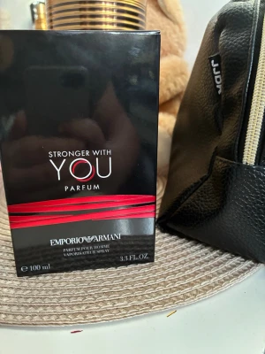 Emporio Armani Stronger With You Parfum - Emporio Armani Stronger With You Parfum är en elegant herrdoft i en mörkbrun glasflaska med silverfärgad rund kork. Förpackningen är svart med röda detaljer och rymmer 100 ml. En stilren och modern parfym som utstrålar lyx och självsäkerhet.