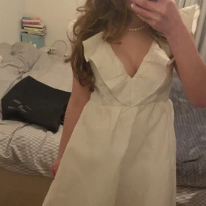 Vit klänning bubbleroom - Supersöt vit kortklänning med djup v-ringning och bred volangkant runt halsen. Klänningen har en liten fläck på framsidan men är annars i mycket gott skick. Klänningen har ett vackert blommigt mönster i tyget och är ärmlös. Perfekt för sommaren och studenten! Tyvärr lite för stor för mig i passformen annars jättefin!!💕