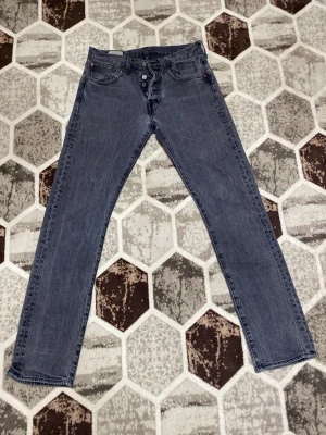 Levi's raka blå jeans med knappar - Klassiska blå jeans från Levi's med raka ben och knappgylf. Jeansen har fem fickor och en röd Levi's-tag på bakfickan. Tillverkade i slitstarkt denimtyg som ger en tidlös look.