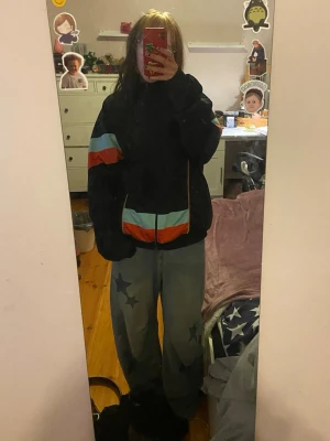 Svart track jacket med färgblock - Svart track jacket från ”Toms” med färgblock i ljusblått och rött på ärmar och midja. Jackan har hel dragkedja, hög krage och ribbade muddar. Perfekt för en sportig och avslappnad stil.