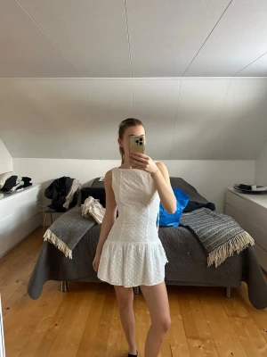 Vit kort klänning med öppen rygg - Superfin vit kort klänning med volangkant och öppen rygg. Klänningen har smala axelband som knyts och ett diskret blommigt mönster i tyget. Underbar studentklänning med ganska tjockt tyg så man alltid känner sig säker med att den ej är genomskinlig etc. 
