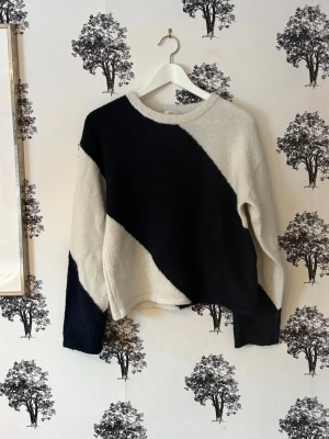 Svartvit stickad tröja med blockmönster - Säljer en stickad tröja i svart och vitt med stora diagonala blockmönster. Tröjan har rund halsringning, långa ärmar och en avslappnad passform. Perfekt för dig som gillar grafiska kontraster och en modern look.