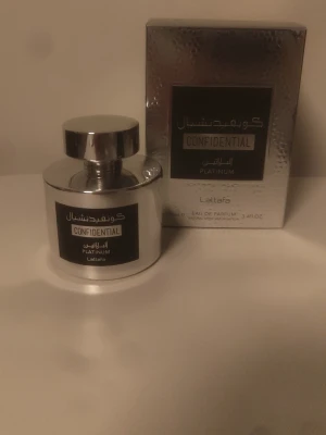 Lattafa Confidential Platinum EDP 100ml - Lattafa Confidential Platinum är en parfym i en snygg, rund silverfärgad flaska med matchande lock. Förpackningen är också silverfärgad med svart etikett och text i både engelska och arabiska. Cirka 97-98ml kvar.