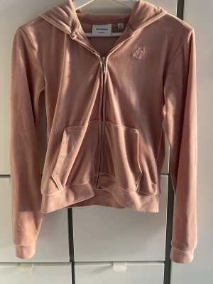 Ljusrosa velour hoodie Juicy Couture - Säljer en ljusrosa hoodie från Juicy Couture med dragkedja och huva. Tröjan är i mjuk velour med broderad JC-logga på bröstet och har två fickor.