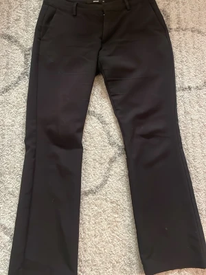 Svarta kostymbyxor  - Snygga svarta kostymbyxor med wida ben och låg midja. Byxorna har hällor för skärp och diskreta fickor fram. Perfekta till en stilren look och passar till många olika outfits. Materialet känns mjukt och följsamt.