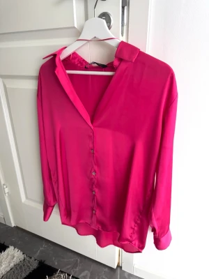 Satinskjorta/blus från Zara - Snygg rosa blus från Zara med v-ringning och knäppning framtill. Lite oversized passform, så hade eventuellt kunnat passa S också. Toppen är i glänsande satinmaterial som ger en lyxig känsla. Aldrig använd! Pris går att diskutera💞
