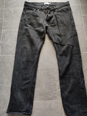 Svarta raka jeans med fickor - Säljer ett par svarta jeans med klassisk femficksmodell och raka ben. Jeansen har bälteshällor, knappgylf och silverfärgade nitar. Materialet är denim i bomull och de har en enkel, stilren look som passar till det mesta.