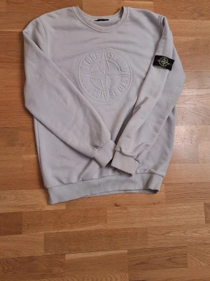 Vit sweatshirt från Stone Island - Säljer en vit sweatshirt från Stone Island med stort broderat logotypmotiv på bröstet och klassisk patch på ärmen. Tröjan har rund hals, ribbade muddar och är tillverkad i mjuk bomull. 