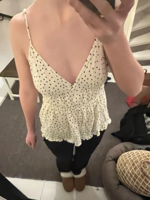 Prickig vit linnetopp med volang - Söt vit linnetopp med svarta prickar och smala axelband. Toppen har v-ringning, volangkant nedtill och smockad rygg för skön passform. Jag bär normalt storlek xs-s, tröjan är m men sitter jättefint på.