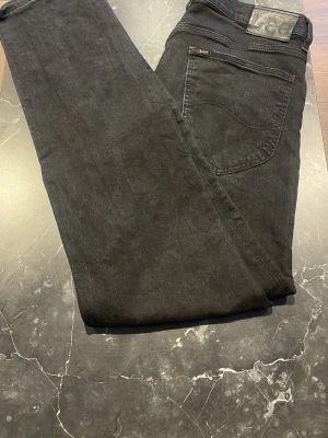Svarta jeans från Lee - Säljer ett par svarta jeans från Lee med klassisk rak passform. Jeansen har fem fickor, Lee-logga på bakfickan och är tillverkade i ett slitstarkt denimtyg. Perfekta för dig som gillar en tidlös och clean stil.