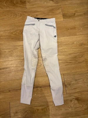 Vita ridbyxor från spooks - Snygga vita ridbyxor från spooks  med ribbade knäpartier och dekorativa mörkblå detaljer vid fickorna. Byxorna har smal passform och stretchigt material som ger bra rörelsefrihet. .