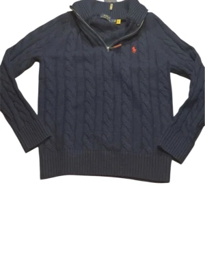 Mörkblå kabelstickad tröja Polo Ralph Lauren - Mörkblå kabelstickad tröja från Polo Ralph Lauren med halv dragkedja och hög krage. Tröjan har ribbade muddar och nederkant,Perfekt för dig som gillar stilren och tidlös design.🫡