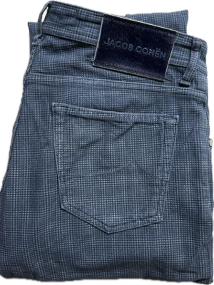 Jacob Cohen Jeans | W34 - Snygga blå jeans från Jacob Cohen med diskret rutmönster i vitt. Nypris ca 5000.  Klassisk femficksmodell med patch i mocka baktill. Tillverkade i mjukt denimtyg som ger en exklusiv känsla. Perfekta för dig som vill ha något unikt i garderoben.