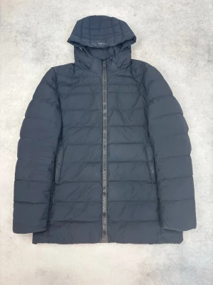 Svart dunjacka från Herno Laminar - Snygg svart dunjacka från Herno Laminar med huva och quiltad design. Jackan har rak passform, dragkedja framtill och diskreta sidofickor. Perfekt för kalla vinterdagar och riktigt stilren look.