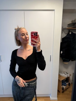 Svart ribbad topp från H&M - Svart långärmad topp från H&M med snygg v-ringning och ribbad struktur. Toppen har en figurnära passform och är perfekt för att lyfta vilken outfit som helst. Enkel men trendig design som passar till mycket.