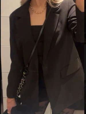 Oversized svart kavaj - Stilren oversized svart kavaj med breda slag och två framfickor. Klassisk design utan synliga knappar framtill. Passar perfekt till en trendig och avslappnad look. Materialet ser ut att vara en mjuk och slät textil.