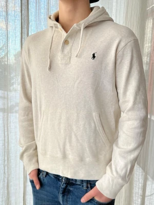 Vit Ralph Lauren hoodie med knappar, storlek M - Vit Ralph Lauren hoodie med knappar och svart logga  100% bomull  Mycket bra skick, något uttöjd i midjan, jättefräsch  Storlek M       Axelbredd: 51 cm Längd: 64 cm