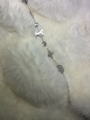 Lv - Armband - Snyggt armband i silverfärg från LV med ikoniska LV-loggan, pärldetaljer och stjärnformade hängen. Kedjan har även runda detaljer och justerbar längd. Perfekt accessoar för att lyfta din outfit. (Inte äkta!)