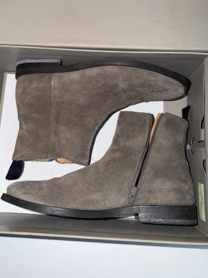 Gråa mockastövlar  från Gant - Snygga gråa stövletter från Gant i mjuk mocka med dragkedja på sidan och svart sula. Klassisk och stilren design som passar till många olika outfits. Skorna har en låg klack och diskret dragflik bak för enkel påtagning.