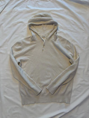 Beige cashmere hoodie från Sayless - Mjuk och stilren beige hoodie från Sayless i lyxigt cashmere-material. Klassisk modell med huva och långa ärmar, perfekt för en avslappnad och trendig look. Ribbstickade muddar vid ärmslut och nederkant ger en snygg finish.