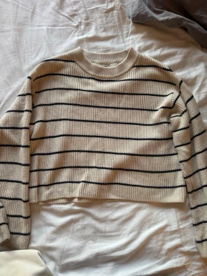 Beige stickad tröja med svarta ränder - Säljer en beige stickad tröja med svarta horisontella ränder. Tröjan har en croppad passform, rund halsringning och långa ärmar. Materialet känns mjukt och ribbstickat, perfekt för lager på lager och en chill look.
