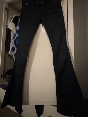 Svarta bootcut jeans med utsvängda ben - Säljer ett par svarta bootcut jeans med riktigt utsvängda ben. Jeansen har klassisk femficksdesign och knappgylf. Snygg passform som sitter tajt upptill och blir bredare nedtill. Perfekta för dig som gillar retrovibbar och vill sticka ut.