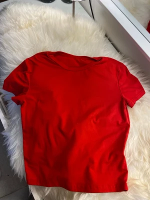 Klassisk röd t-shirt i bomull - En enkel och stilren röd t-shirt med rund hals och korta ärmar. Perfekt basplagg som passar till det mesta och är skön att bära tack vare mjukt bomullsmaterial.