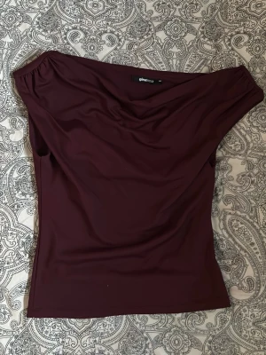 Vinröd topp Gina Tricot - Säljer en vinröd (off shoulder på ena sidan) topp från Gina Tricot. Toppen har en draperad urringning och är figurnära i modellen. Använd 1 gång så nästan helt ny.