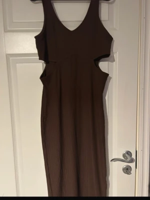 Brun ribbad långklänning med trendiga cut-outs - Stilren brun långklänning med ribbad struktur och snygga cut-outs som ger en modern och trendig Ärmlös modell med v-ringning Både bekväm och statement på samma gång perfekt till middag, fest eller semester ✨(ifrån h&m) 