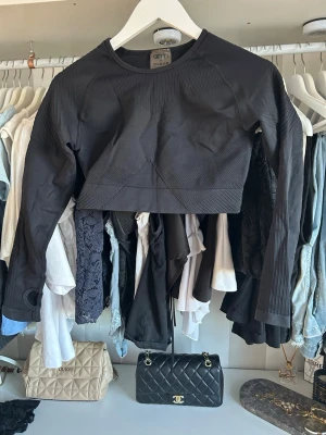 Svart croppad långärmad topp Aim'n - Säljer en svart croppad långärmad topp från Aim'n. Toppen har rund halsringning, ribbade detaljer och är tillverkad i ett stretchigt syntetmaterial som passar perfekt till träning. Snygg och sportig design med tumhål i ärmsluten.