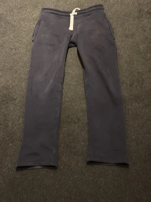 Russemerch byxor  - Mörkblå mjukisbyxor från R i storlek XS. Byxorna har raka ben, två sidofickor och en vit dragsko i midjan. Tillverkade i mjukt och skönt material som passar perfekt för chill dagar. Klassisk och enkel design.