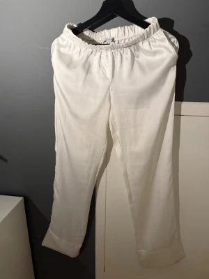 Vita linnebyxor med resårmidja - Säljer ett par vita linnebyxor med avslappnad passform och bred resår i midjan. Byxorna har raka ben och är tillverkade i ett lätt och luftigt linnematerial, perfekta för en chill och stilren look. Inga synliga fickor eller detaljer.