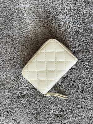 Beige quiltad plånbok med dragkedja - Snygg beige plånbok i quiltad design med dragkedja runtom. Plånboken har flera fack för kort och ett myntfack med egen dragkedja. Perfekt storlek för att ha med sig i väskan och håller ordning på dina kort och kontanter.