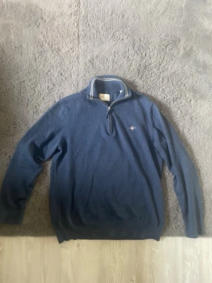 Marinblå halvzip tröja från Gant - Snygg marinblå tröja från Gant med halv dragkedja. Köpt för 1700kr. Använd 1 gång då den var för liten när jag köpte den. Är M storlek men skulle nog säga S. Vid frågor är det bara att skriva.