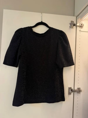 Svart glittrig blus med puffärm - Snygg svart topp med glittrigt material och puffiga ärmar. Perfekt för en enkel men ändå festlig look. 🩷🩷 använd 1 gång så mycket bra skick!