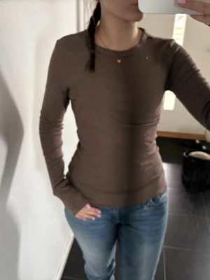 Brun långärmad topp - Snygg brun långärmad topp med rund halsringning och figurnära passform. Använd fåtal ggr. Perfekt att styla med jeans eller kjol för en enkel och clean look. Materialet känns mjukt och stretchigt, vilket gör den bekväm att bära hela dagen.