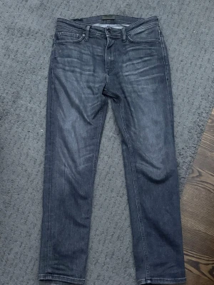 Grå raka jeans regular fit - Säljer ett par grå jeans med rak passform från Jack and Jones. Jeansen har en diskret tvättad look och silverfärgade nitar. Perfekta för en avslappnad stil och passar till det mesta. Materialet känns mjukt och följsamt. Storlek 29, 30